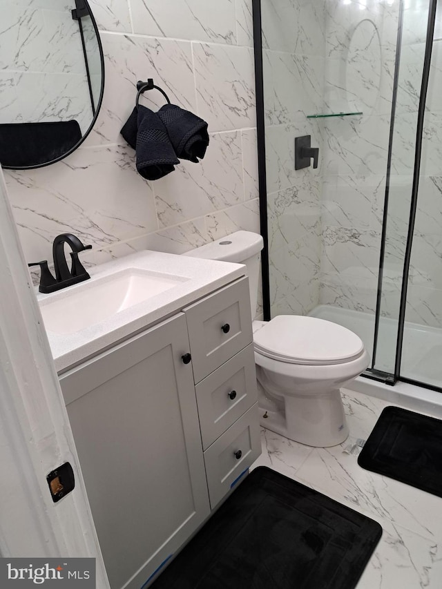 bathroom with a shower with door, vanity, tile walls, and toilet