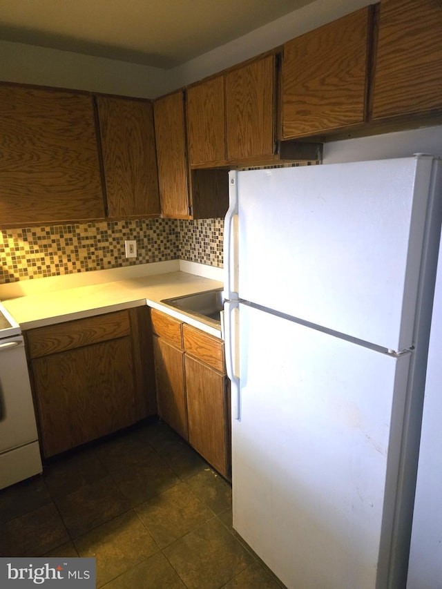 kitchen with backsplash, sink, dark tile patterned flooring, range, and white fridge