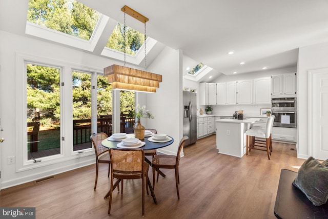 dining room with high vaulted ceiling, a skylight, and light hardwood / wood-style flooring