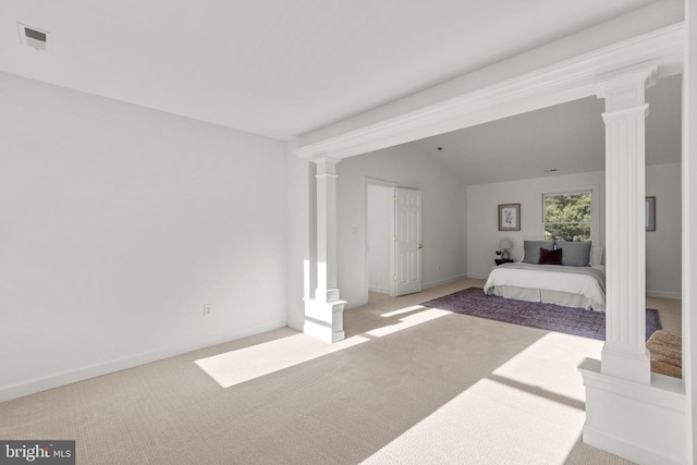 unfurnished bedroom with decorative columns, light colored carpet, and vaulted ceiling