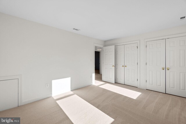 unfurnished bedroom featuring light colored carpet and multiple closets