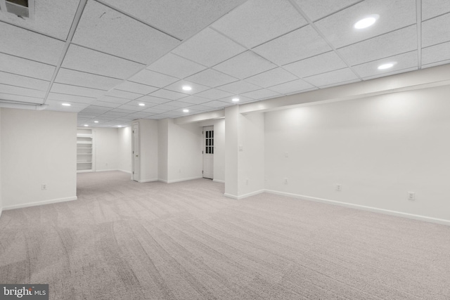 basement with a paneled ceiling and light carpet