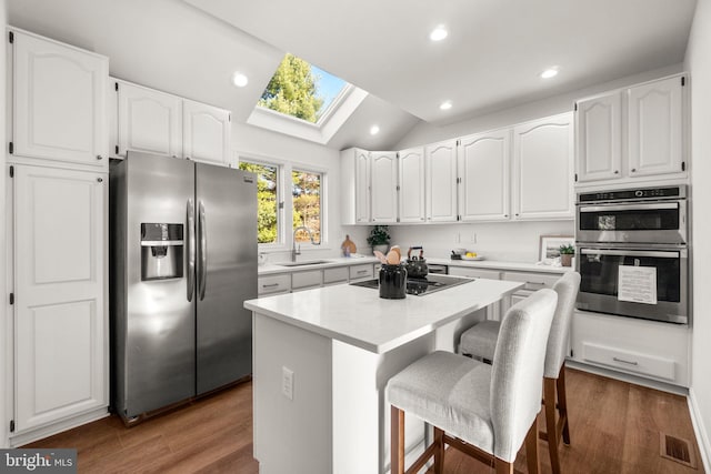 kitchen featuring a breakfast bar, a center island, lofted ceiling with skylight, white cabinets, and stainless steel appliances