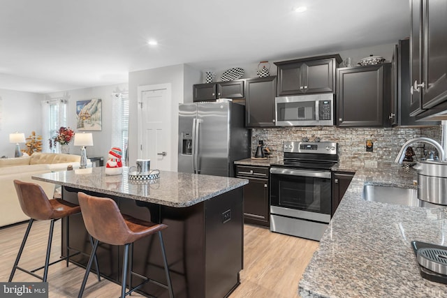 kitchen featuring light stone countertops, appliances with stainless steel finishes, sink, a center island, and a breakfast bar area