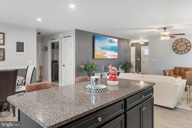 kitchen featuring ceiling fan, a center island, a kitchen breakfast bar, dark stone countertops, and light wood-type flooring