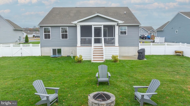 back of house featuring a sunroom, a yard, and a fire pit