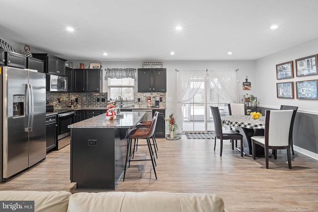 kitchen featuring light stone counters, light hardwood / wood-style floors, a breakfast bar, a kitchen island, and appliances with stainless steel finishes