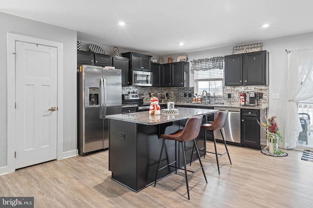 kitchen featuring light stone countertops, appliances with stainless steel finishes, a breakfast bar, light hardwood / wood-style flooring, and a center island