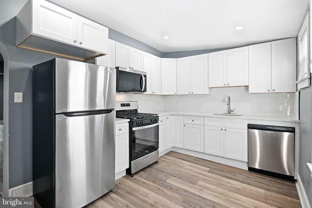 kitchen with sink, tasteful backsplash, appliances with stainless steel finishes, white cabinets, and light wood-type flooring