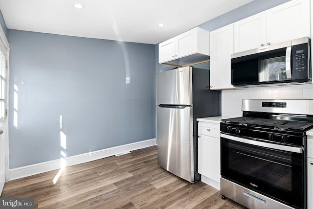 kitchen featuring white cabinets, backsplash, stainless steel appliances, and hardwood / wood-style flooring