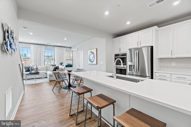 kitchen with appliances with stainless steel finishes, a kitchen breakfast bar, sink, light hardwood / wood-style flooring, and white cabinetry