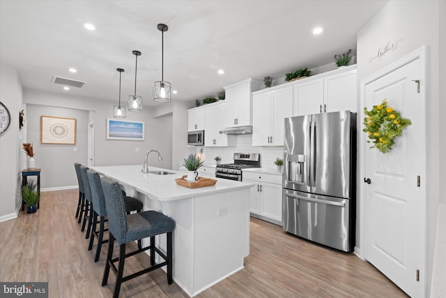 kitchen featuring white cabinetry, sink, hanging light fixtures, an island with sink, and appliances with stainless steel finishes