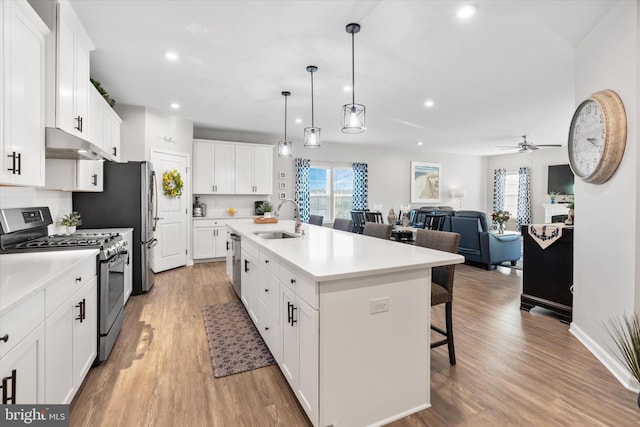 kitchen with stainless steel appliances, ceiling fan, sink, white cabinets, and an island with sink