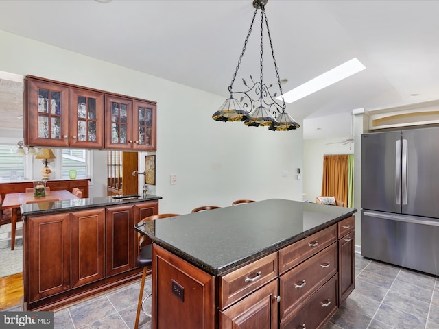 kitchen with a breakfast bar area, stainless steel fridge, hanging light fixtures, a center island, and ceiling fan