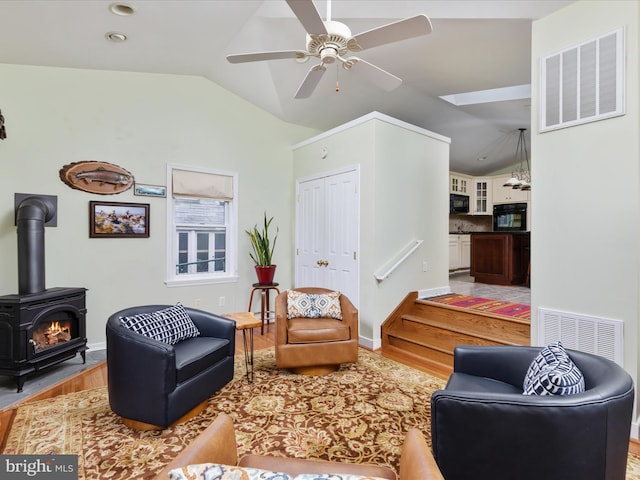 living room with vaulted ceiling, a wood stove, hardwood / wood-style floors, and ceiling fan