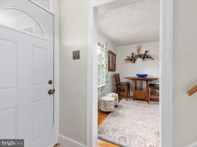 foyer entrance with wood-type flooring, crown molding, and a textured ceiling