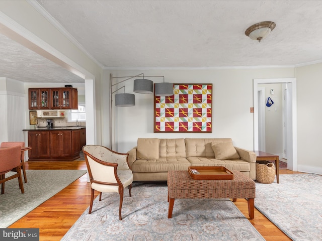 living room featuring indoor bar, ornamental molding, a textured ceiling, and light wood-type flooring