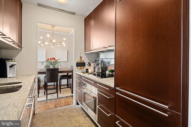 kitchen with light stone countertops, a notable chandelier, refrigerator, oven, and black electric stovetop