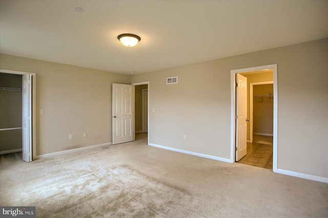 unfurnished bedroom with light carpet and a walk in closet