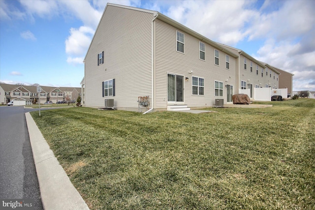 back of house with central AC unit and a yard