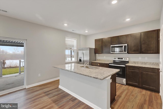 kitchen with sink, light hardwood / wood-style flooring, an island with sink, dark brown cabinets, and appliances with stainless steel finishes