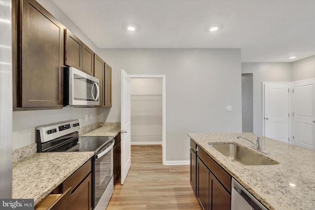 kitchen with appliances with stainless steel finishes, light stone counters, dark brown cabinetry, sink, and light hardwood / wood-style flooring