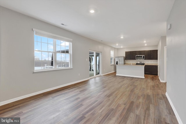 kitchen featuring dark brown cabinets, stainless steel appliances, dark hardwood / wood-style floors, and an island with sink