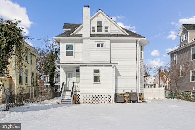 snow covered rear of property featuring central AC