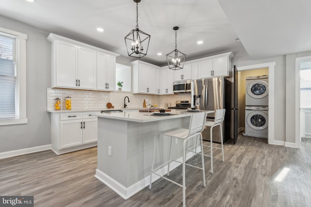 kitchen with a center island, hanging light fixtures, stacked washer and dryer, white cabinets, and appliances with stainless steel finishes