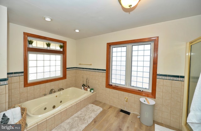 bathroom with hardwood / wood-style floors, tile walls, and tiled tub