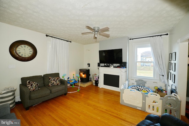 living room featuring ceiling fan, wood-type flooring, a textured ceiling, and a wood stove