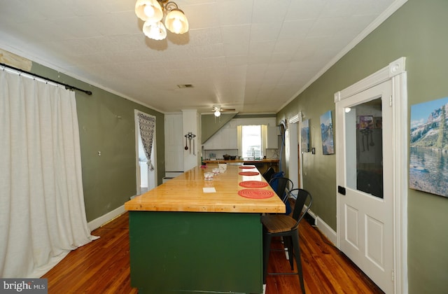 kitchen with dark hardwood / wood-style floors, crown molding, ceiling fan, and a breakfast bar area