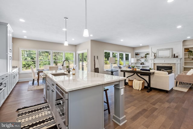 kitchen featuring dark wood-type flooring, light stone countertops, a center island with sink, and pendant lighting