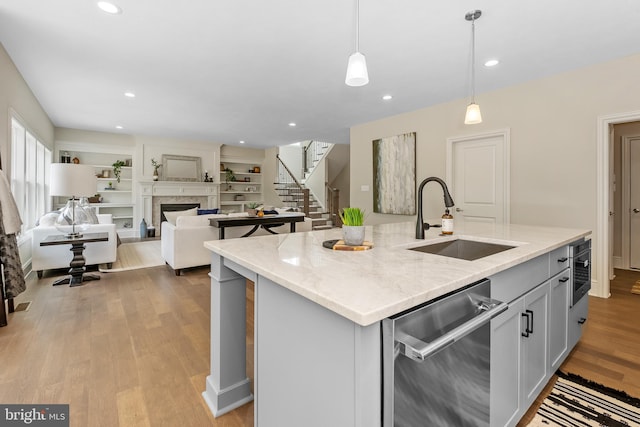 kitchen featuring light stone counters, stainless steel dishwasher, a kitchen island with sink, sink, and hanging light fixtures