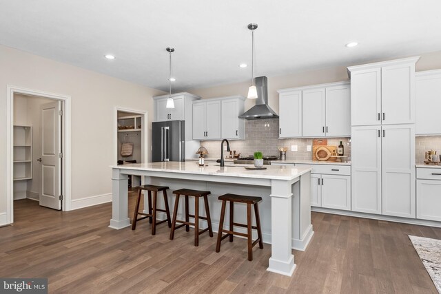 kitchen with a center island with sink, wall chimney exhaust hood, white cabinets, and decorative light fixtures