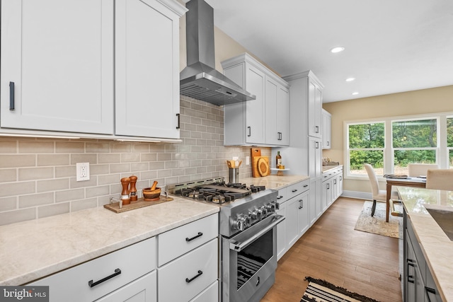 kitchen with white cabinets, wall chimney range hood, decorative backsplash, high end stove, and light hardwood / wood-style floors