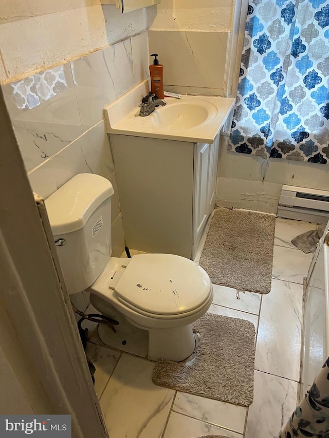 bathroom with toilet, vanity, baseboard heating, and tile walls
