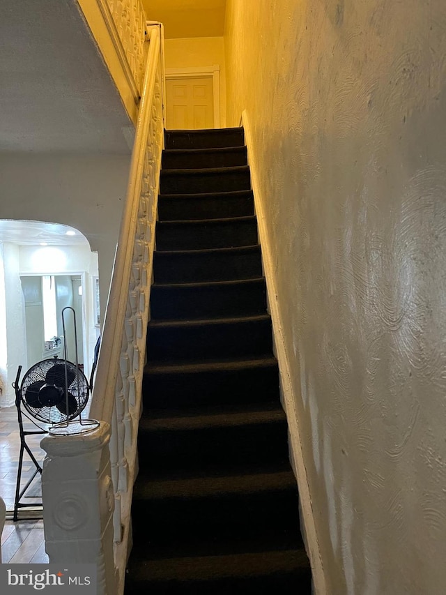 stairs featuring arched walkways and wood finished floors