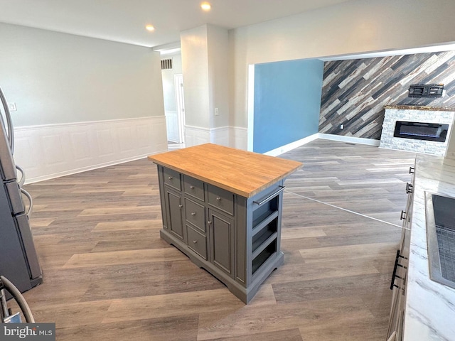 interior details with wainscoting, wood finished floors, freestanding refrigerator, a fireplace, and recessed lighting