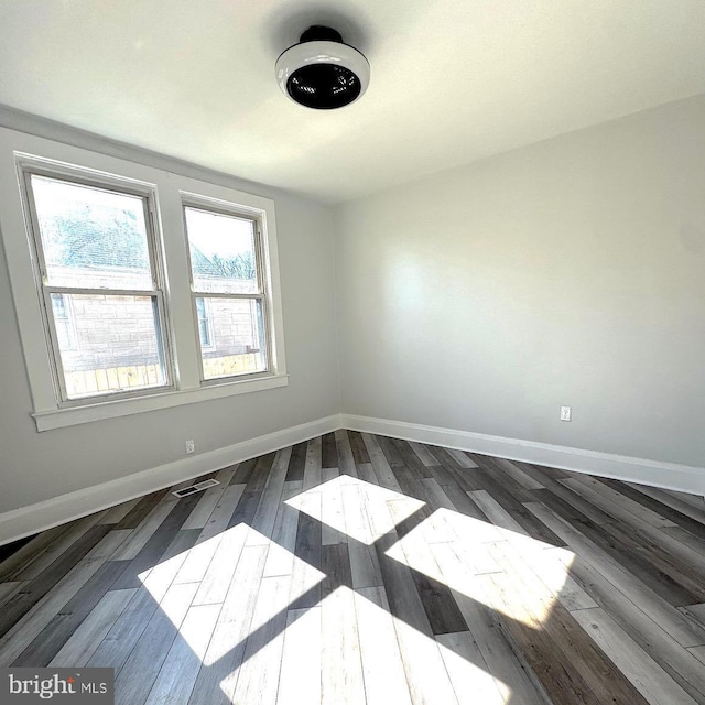 unfurnished room featuring visible vents, dark wood finished floors, and baseboards