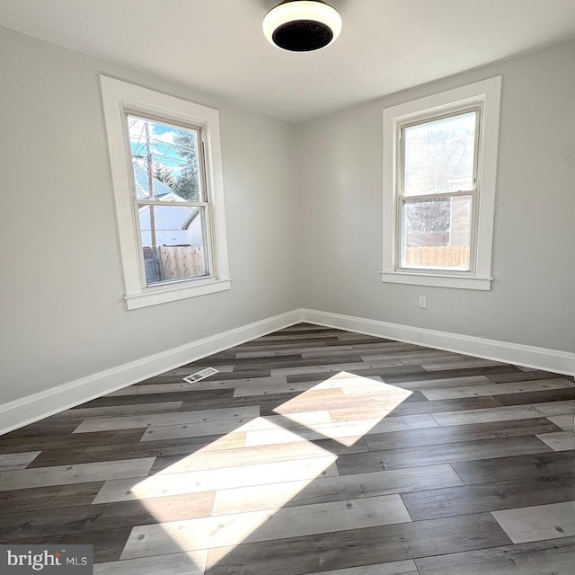 spare room featuring visible vents, baseboards, and dark wood finished floors