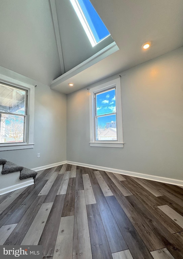 empty room with vaulted ceiling with skylight, dark wood finished floors, a wealth of natural light, and baseboards