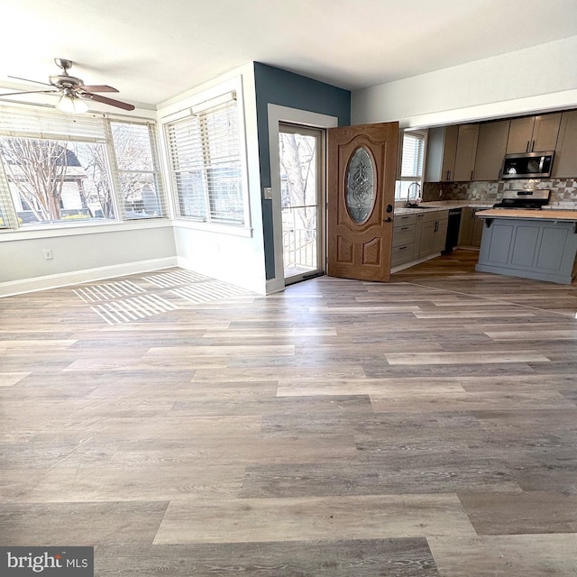 kitchen with light wood finished floors, stainless steel appliances, light countertops, open floor plan, and a sink