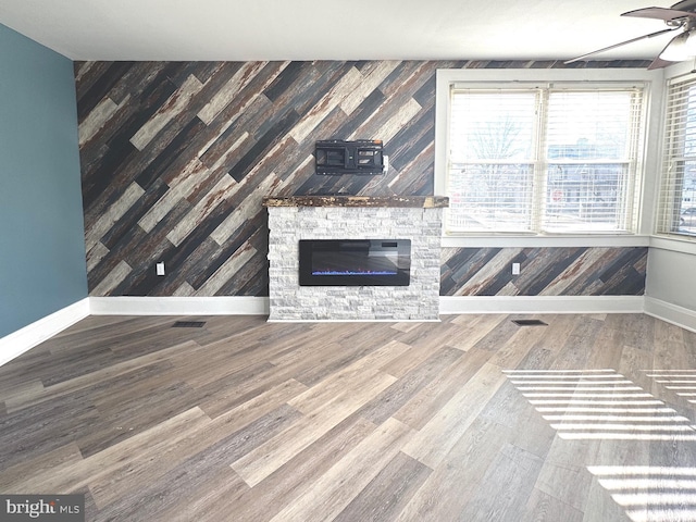 unfurnished living room featuring a fireplace, visible vents, ceiling fan, wood finished floors, and baseboards