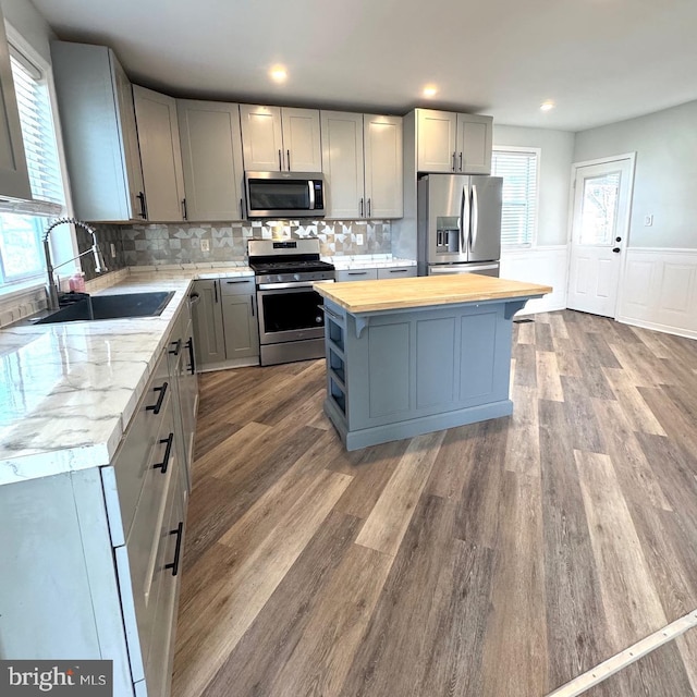 kitchen featuring butcher block counters, gray cabinets, appliances with stainless steel finishes, a sink, and a kitchen island