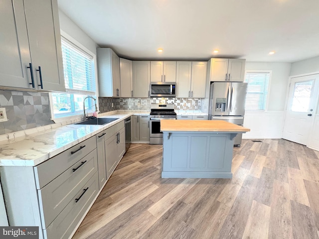 kitchen with gray cabinetry, stainless steel appliances, a sink, and a center island