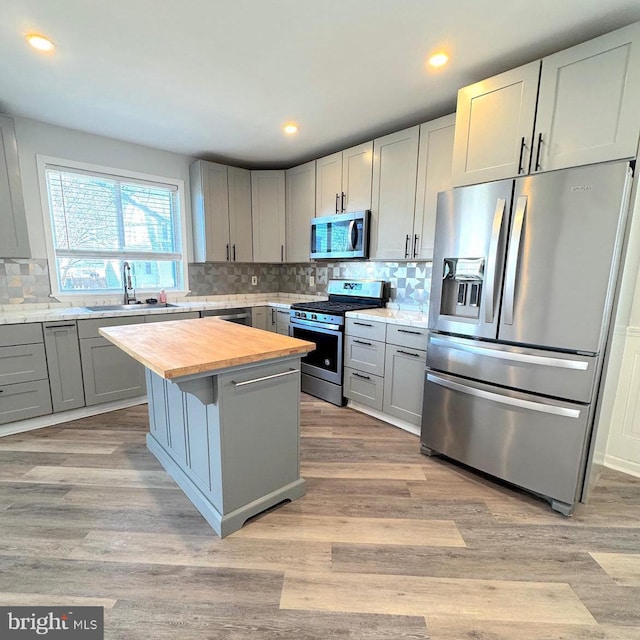 kitchen featuring gray cabinets, appliances with stainless steel finishes, a sink, wood counters, and a kitchen island