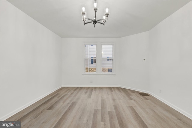 spare room with light wood-type flooring and a notable chandelier