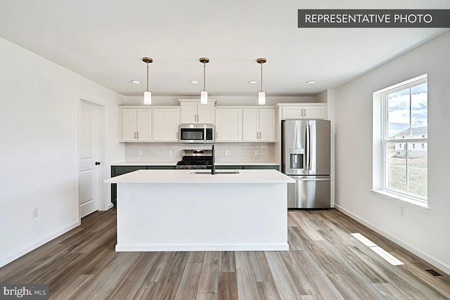 kitchen featuring stainless steel appliances, a kitchen island with sink, sink, decorative light fixtures, and white cabinets