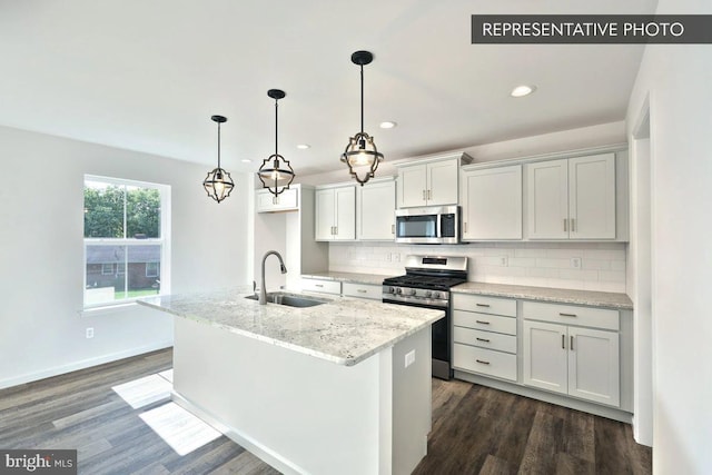 kitchen with a kitchen island with sink, sink, appliances with stainless steel finishes, tasteful backsplash, and light stone counters